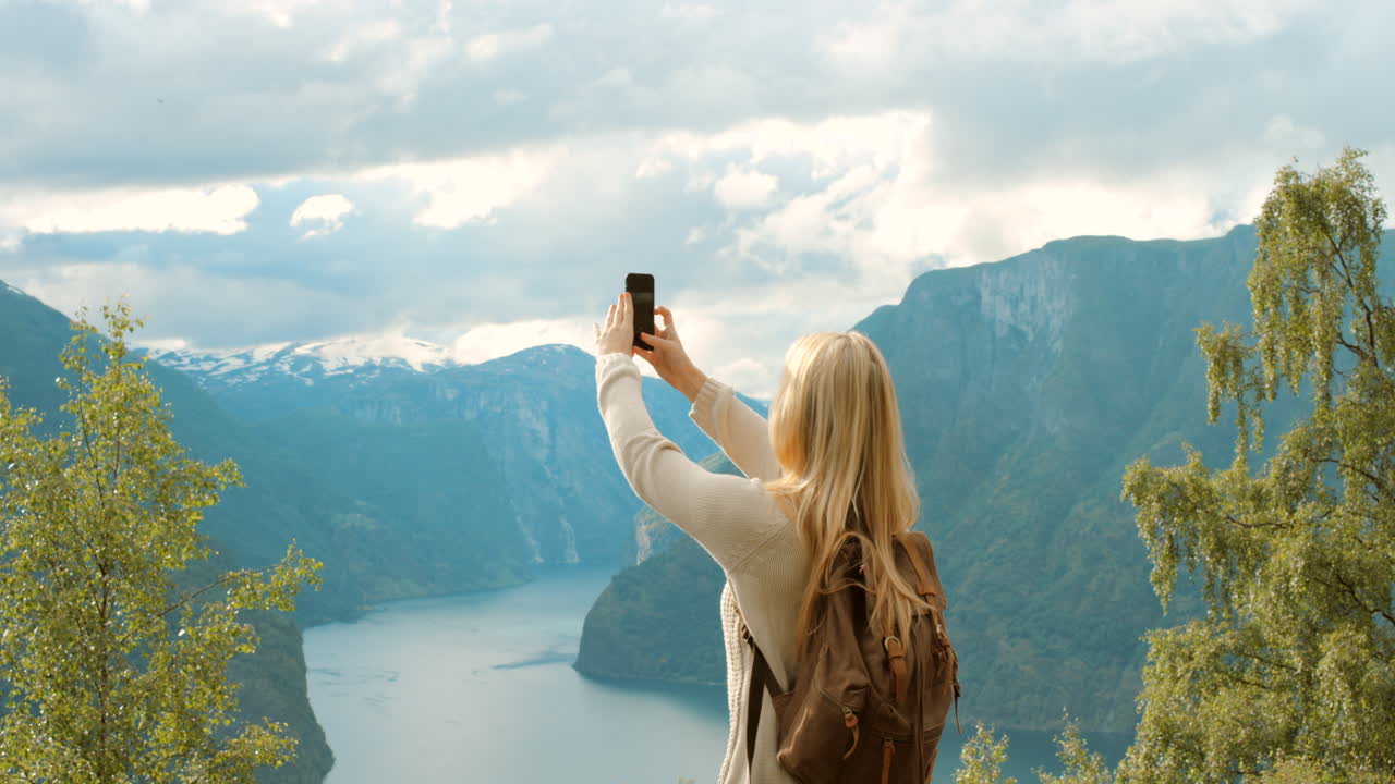 mujer tomando una foto de un fiordo noruego
