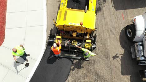 aerial top down, construction workers operate asphalt paver to pave new road