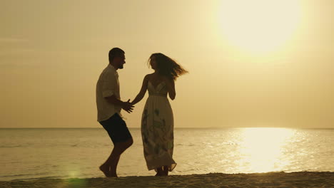 silhouettes of a young couple cool dancing against the backdrop of the sea and the setting sun merry