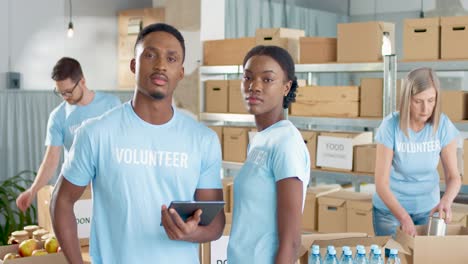 african american young male and female volunteers typing on tablet and smiling at camera