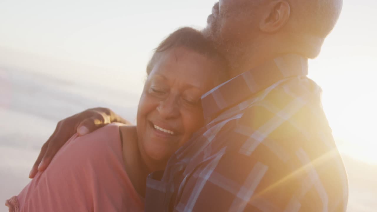 una pareja de ancianos afroamericanos sonrientes abrazándose juntos en una playa soleada