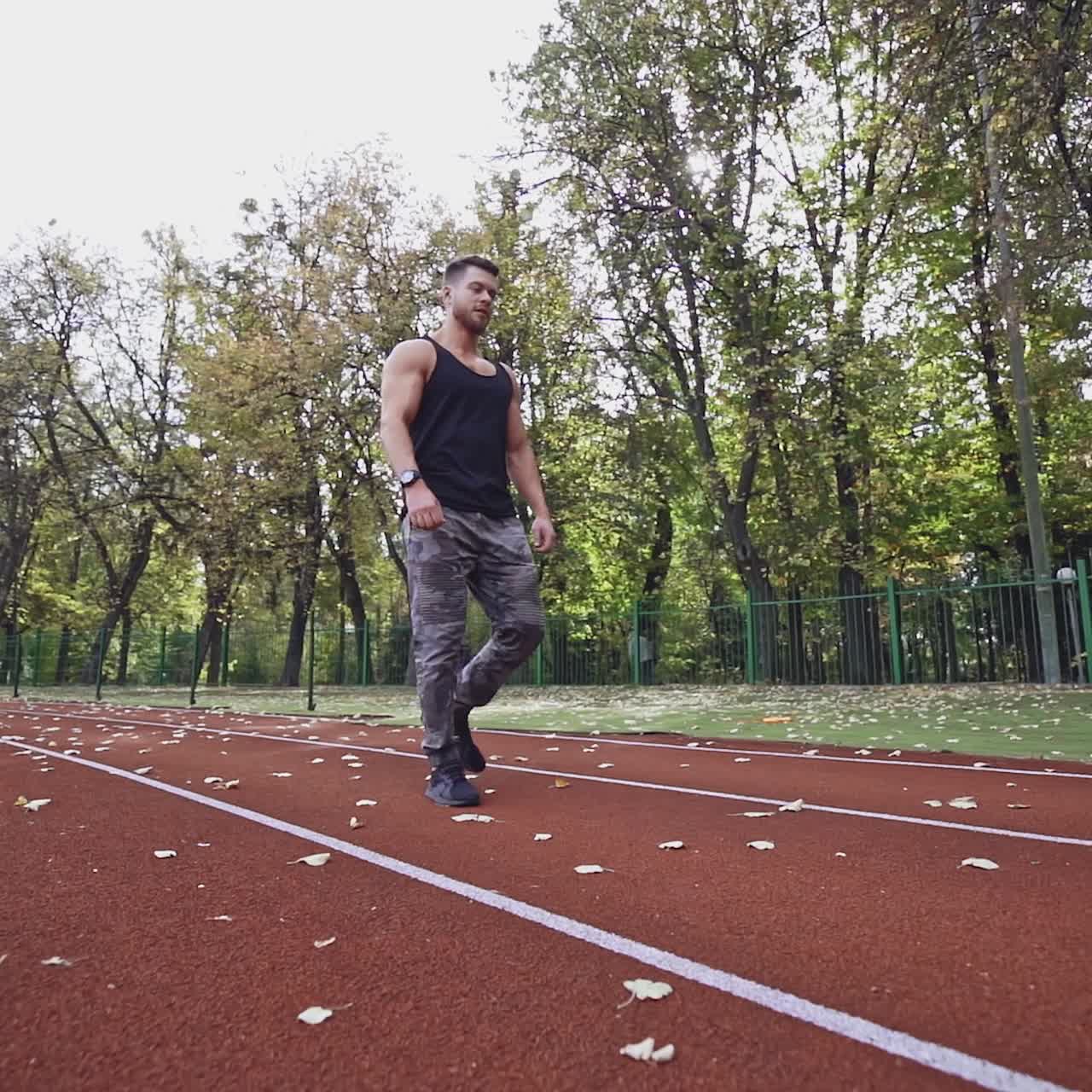 Healthy athlete walking on the modern stadium. Handsome sportsman lifting heavy weights on the nature background. Slow motion.