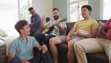 Happy-diverse-male-friends-playing-guitar-and-talking-in-living-room