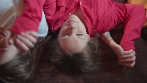 three young women preparing to rest backward on brown bedspread in warm wooden room, seen from behind, casual clothing and relaxed body language capturing mood of comfort