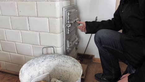 man brushes off his dirty hands and closes door of an old home tiled stove