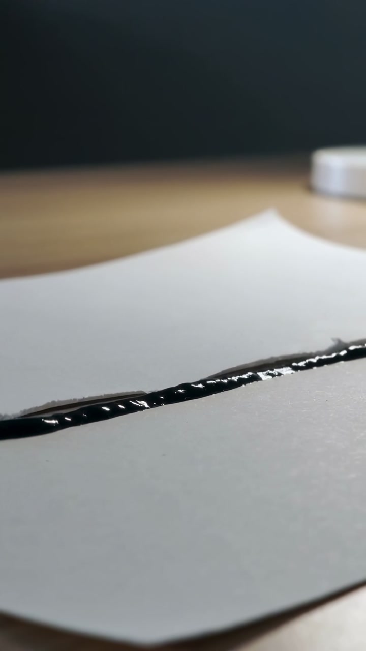 Vertical video: Marker tip touching slit drawing wet ink along tear to highlight design