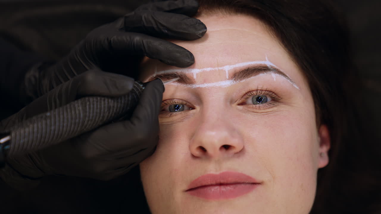 Hands of cosmetologist in black gloves hold the special tool for permanent eyebrow make up. Close up. Blurred backdrop.