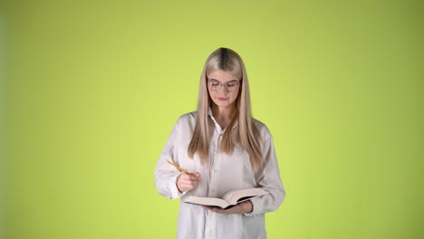 young blonde lady writing on notepad book then looking at camera, studio shot of educational illustration