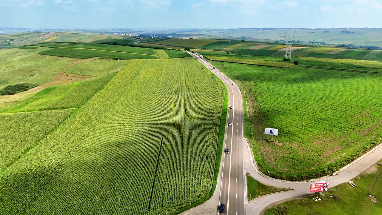Green fields by winding road. Vast green fields stretch out beside a paved road, showcasing farmland and distant hills under a bright sky
