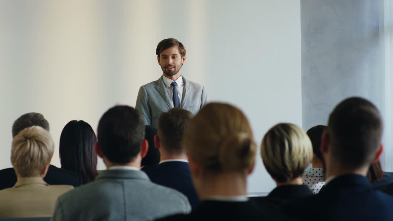Caucasian businessman speaker on a podium wearing formal clothes and talking in a conference room in front to many people