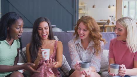 multi-cultural group of women sitting on sofa at home admiring friends engagement ring