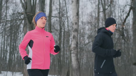 young man and woman on a morning run in the winter forest. a woman in a loose jacket a man in a black jacket is running through a winter park. healthy lifestyle happy family.