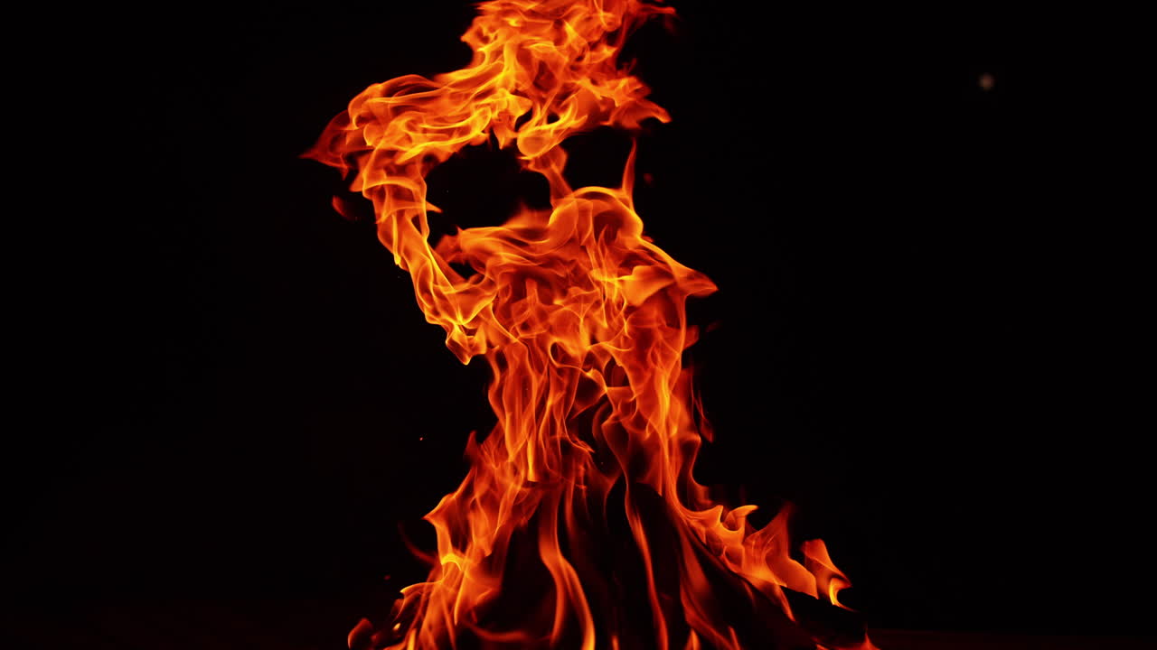 Campfire flames rising high into the darkness. Isolated bonfire burning on the ground.
