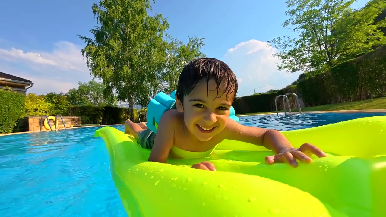 Happy Young Boy Smiling on Inflatable Raft in Swimming Pool