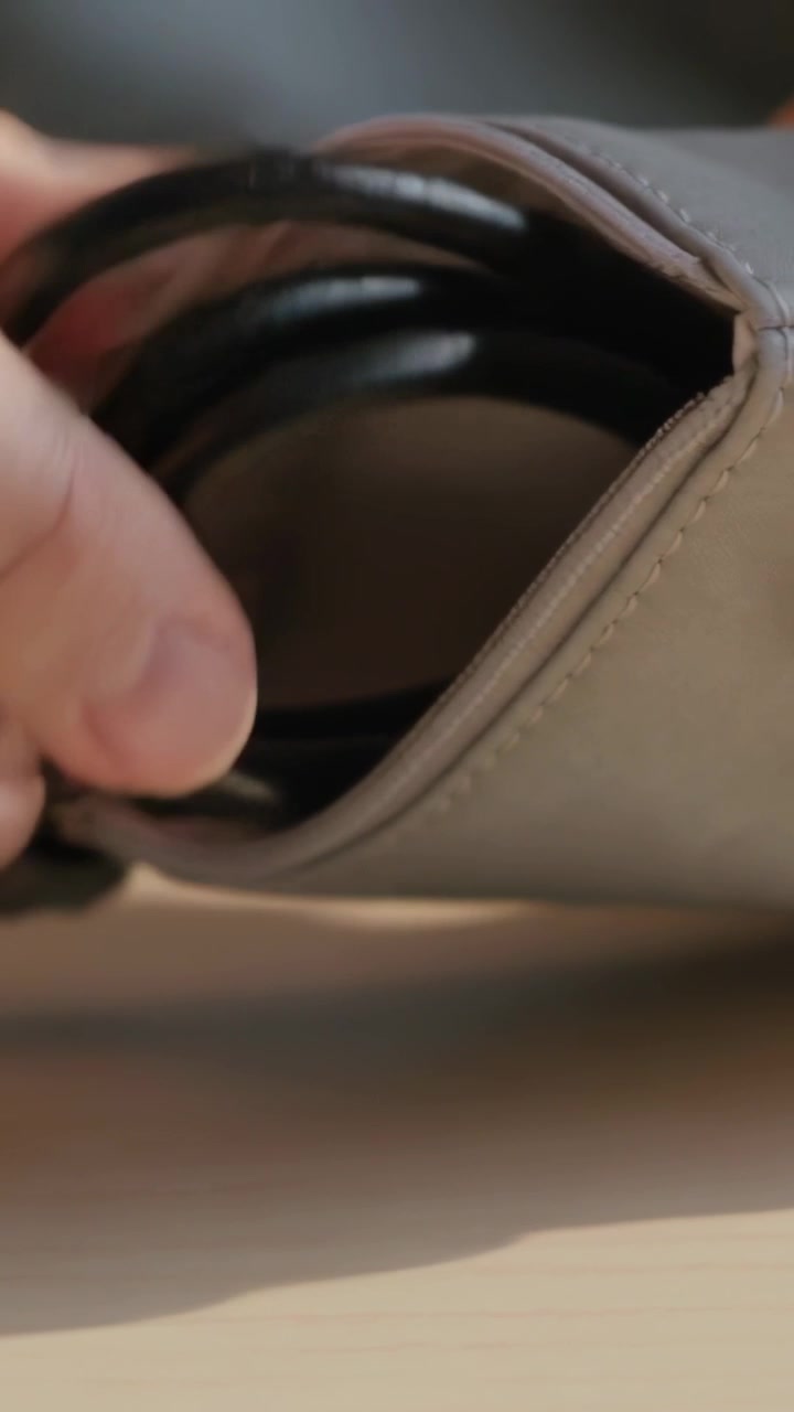 Video vertical: Manos entrando por la izquierda examinando una bolsa beige sobre la mesa, guardando un cable negro para almacenar.