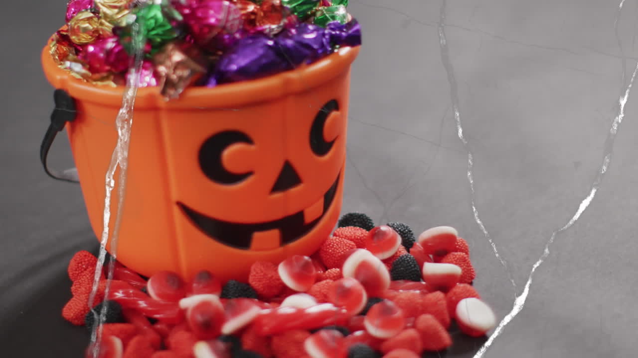 Animation of halloween carved pumpkin bucket with sweets on grey background