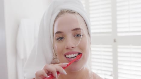 retrato de una feliz mujer caucásica de talla grande con una toalla en la cabeza cepillándose los dientes en cámara lenta