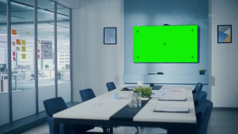 modern empty meeting room with big conference table with various documents and laptops on it, on the wall big tv with green chroma key screen. contemporary scandinavian style designed work environment