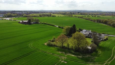 Rural-British-farmhouse-aerial-view-surrounded-by-lush-green-trees-and-agricultural-meadow-farmland-countryside