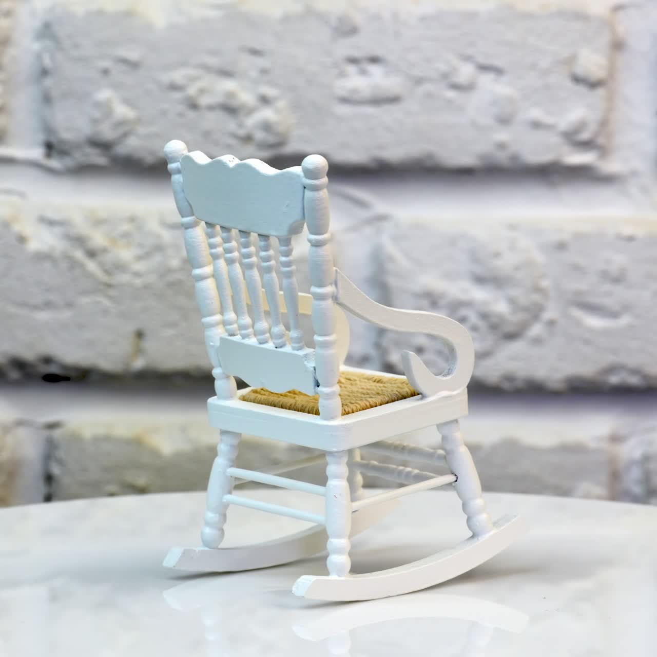 Little white rocking chair for doll's house. Pretty small piece of furniture on the rotating table. White brickwall at the background. Close up