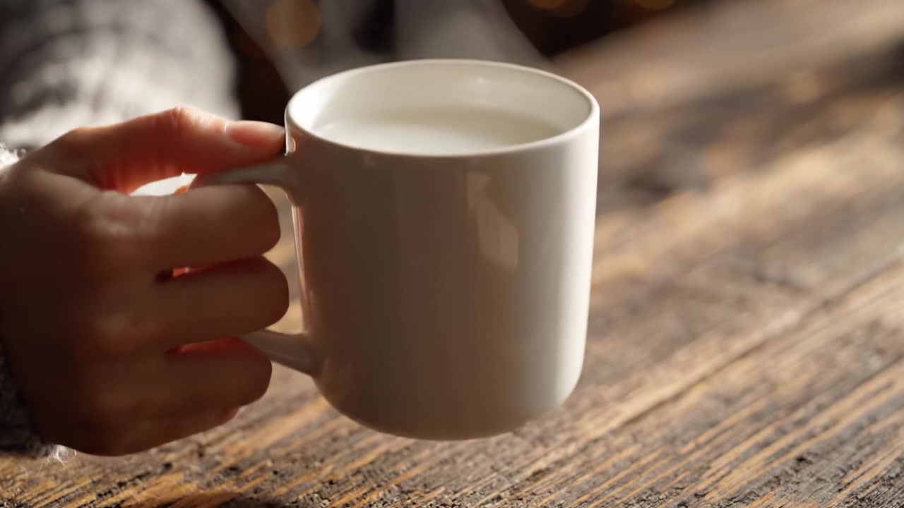 Warm Comfort: A Close-Up of a Steaming Mug of Milk Held in Hand Against a Rustic Wooden Background, Evoking a Cozy Atmosphere Perfect for Relaxation