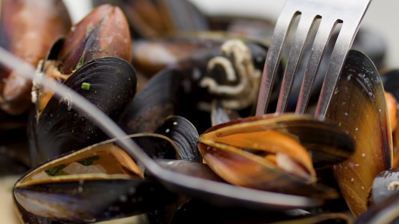 Nahaufnahme von gedämpften Muscheln, die mit Besteck gegessen werden, natürliches Licht, geringe Schärfentiefe