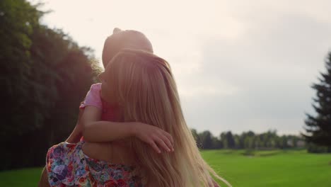 joyful woman circling girl in her arms in garden. mother picking up daughter.