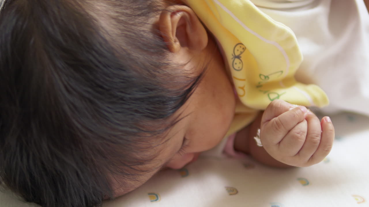 Watch as this Asian infant successfully rolls over on her mattress, highlighting the exciting stages of baby development and the joy of reaching new milestones.
