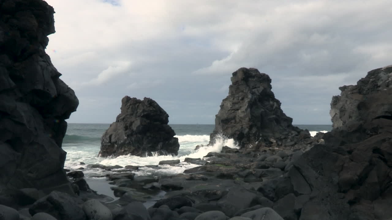 волны разбиваются о вулканические морские стеки на пляже в рибейра-гранде, португалия