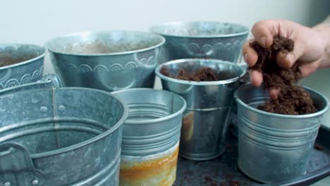 with a tattooed arm, a man is spreading the soil across the buckets, distributing it evenly as he goes