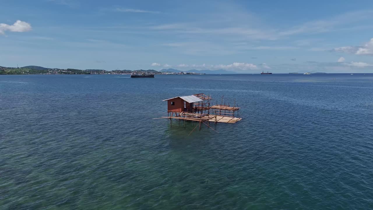 A wooden fisherman's hut on stilts in shallow waters with mountainous landscape in the distance