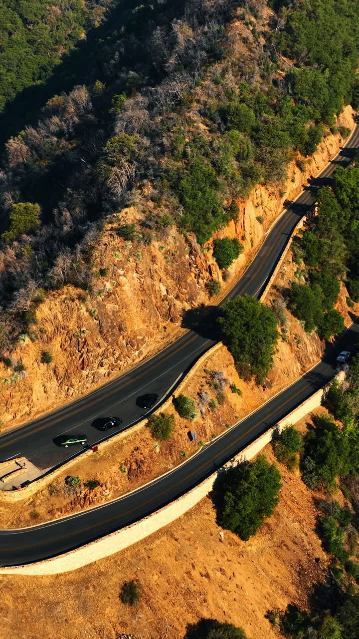 Highway turn on the mountain top. Some cars stand on the road near the slope. Drone footage on sunny day. Vertical video