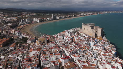 sweeping aerial of peniscola castle peninsula and beachfront under a clear blue sky