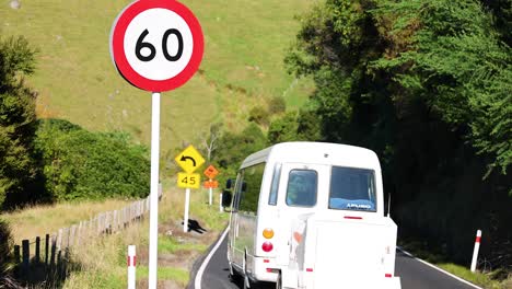 vehicles travel along a winding road in akaroa, surrounded by lush greenery under bright daylight