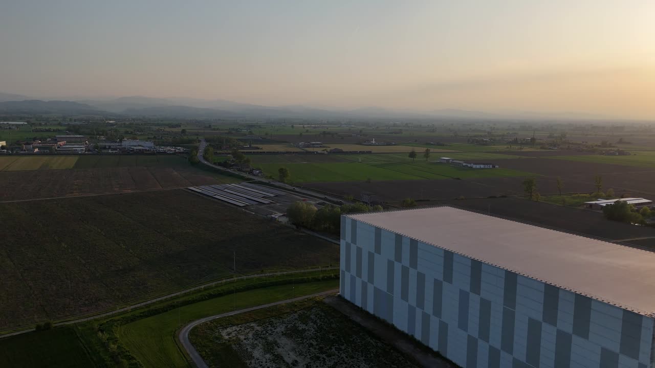 Moderne datacenterbygning i et landligt Po-dalen landskab med tilstødende solcellepark under opførelse og fjerne Apenninerne, der danner en diset baggrund under varmt solnedgangslys