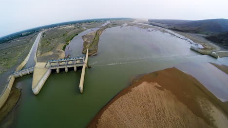 Aerial-view-of-spillway-of-a-dam,-Green-water-in-the-dam,-The-dam-has-partial-dry-surface