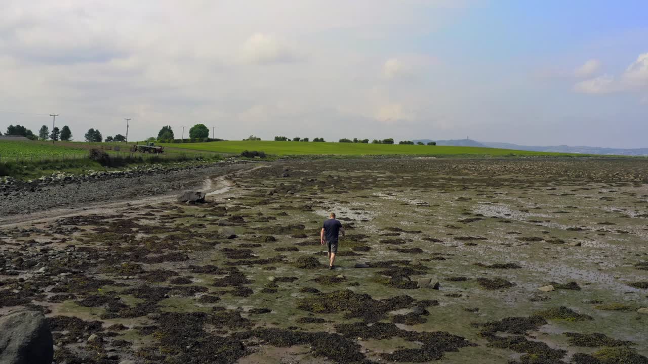 Seorang pria berjalan di sepanjang garis pantai di pantai yang tertutup rumput laut
