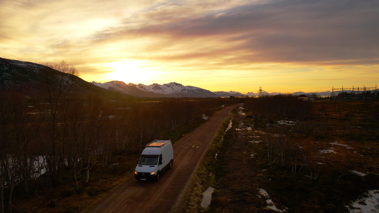 Aerial view of a van driving down a dirt road at sunset on an adventure in remote land with mountains and light snow cover