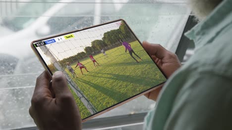 african american man using tablet with diverse male soccer players playing match on screen