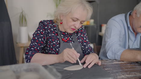 a group of elderly people at a master class in pottery together sculpt and cut a drawing on cups of clay for the manufacture of ceramic dishes