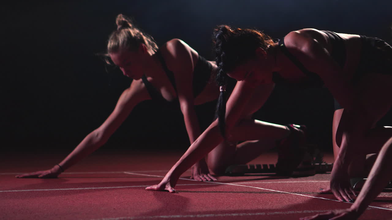tres chicas con ropa negra están en las plataformas de salida para comenzar la carrera en la competencia a la luz de las linternas.