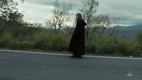 enigmatic secure woman walks with a long black cloak in the mountain road