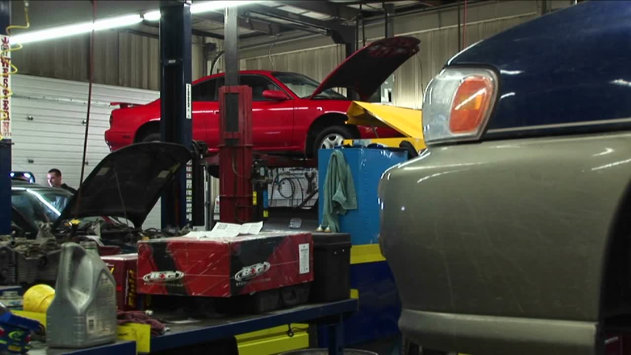 수리를 위해 차를 들고 있는 미디엄 샷과 배경에 있는 고객이 정비사와 이야기합니다.