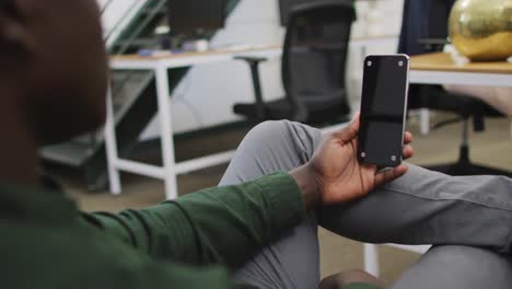 hombre de negocios afroamericano feliz usando un teléfono inteligente con espacio de copia en la oficina