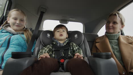 Carefree-cheerful-company-rides-in-the-back-seat-of-the-car.-Mother-with-two-children