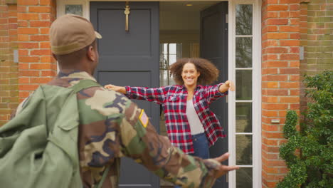 American-Soldier-In-Uniform-Returns-Home-To-Family-On-Leave-Hugging-Wife-And-Children-Outside-House