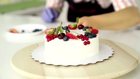 the girl, the chief confectioner, decorates forest berries, strawberries, a homemade cake