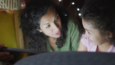 Mixed-race-mother-and-daughter-using-tablet-in-blanket-tent