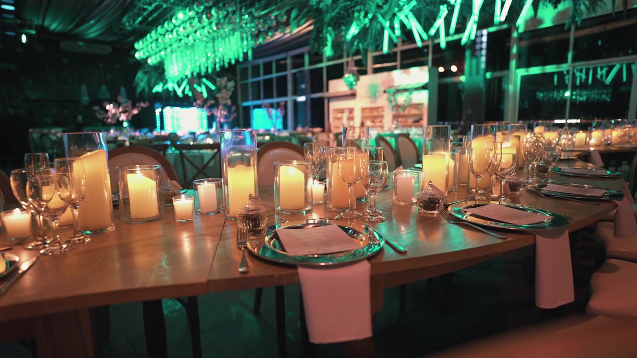A warmly lit dining area with candles and elegant table settings under green ambient lighting. Suitable for event planning visuals or luxury dining promotions.