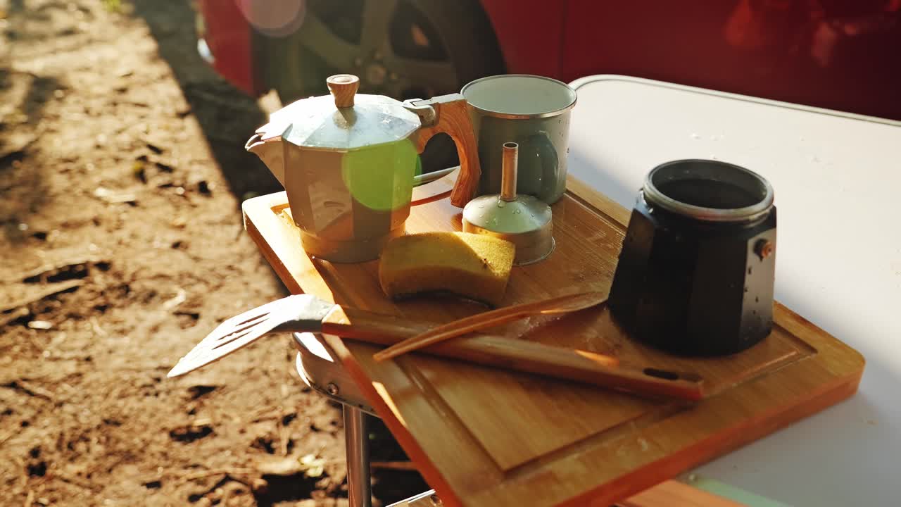 Slow motion close up of vintage coffee pot and camping utensils glowing, sunset